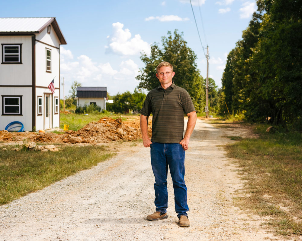 Person stands on dirt roadway in front of structures under construction.