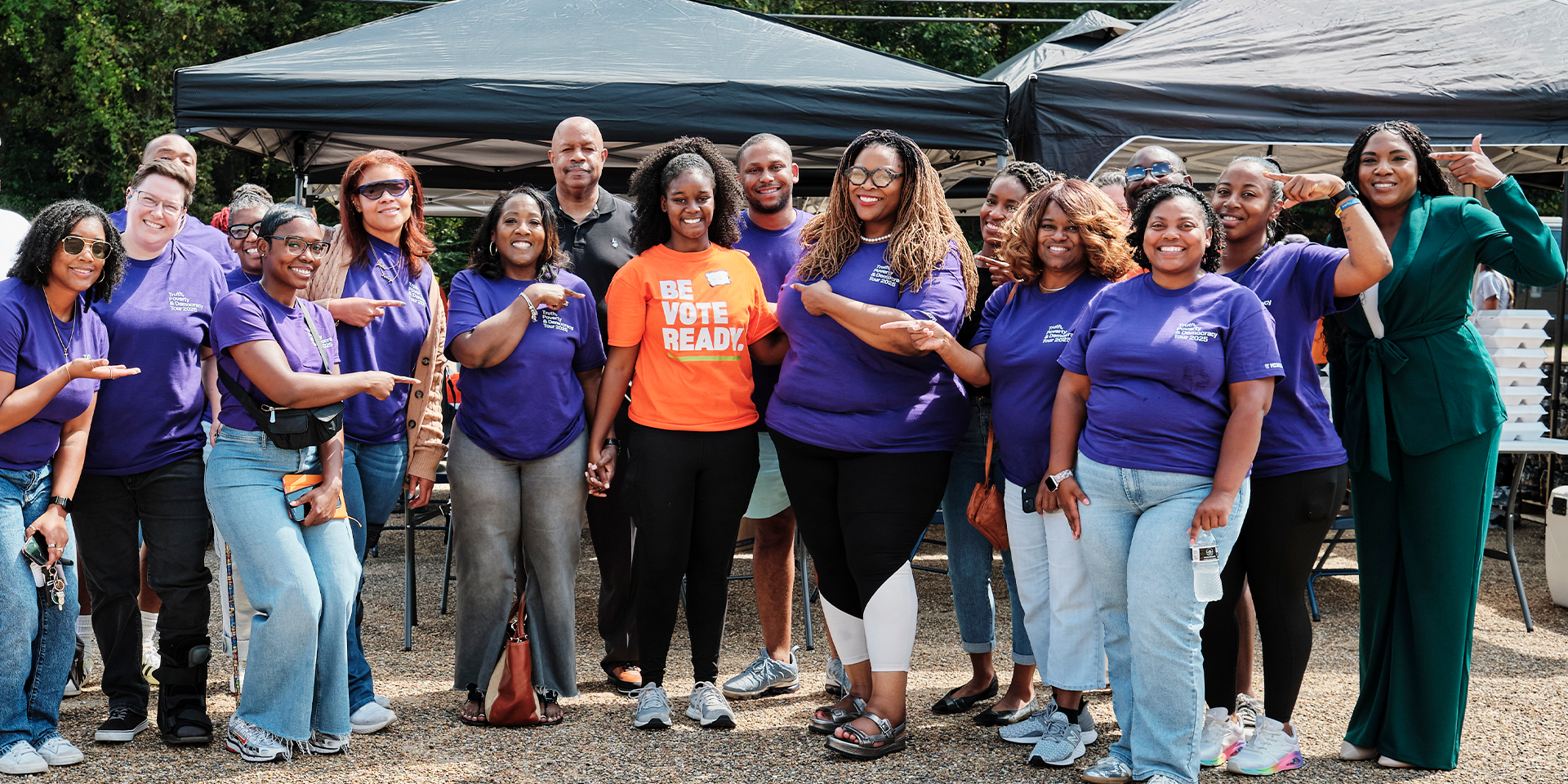 Group photo of volunteers in purple shirts. Person in center wears an orange shirt that says, 'Be Vote Ready.'