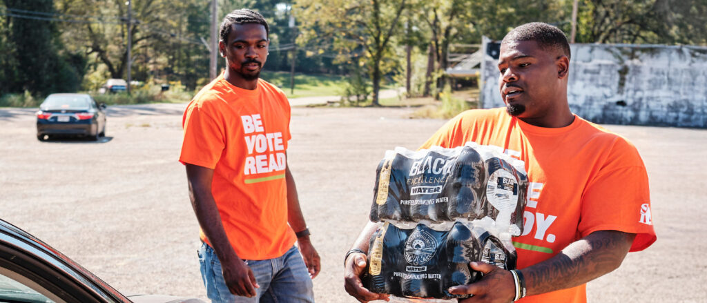 People carry water bottle cases to car.