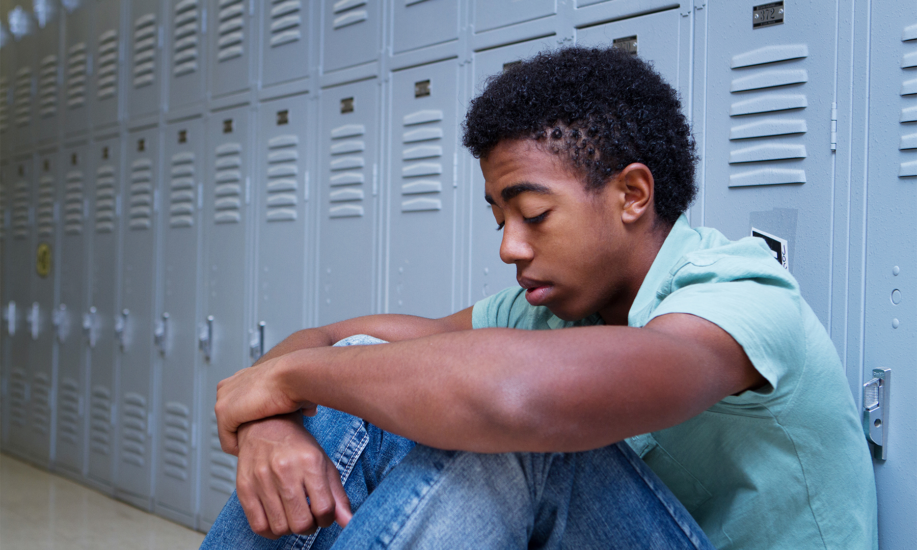 Sad African American student sitting against lockers | Hate at School May 2018
