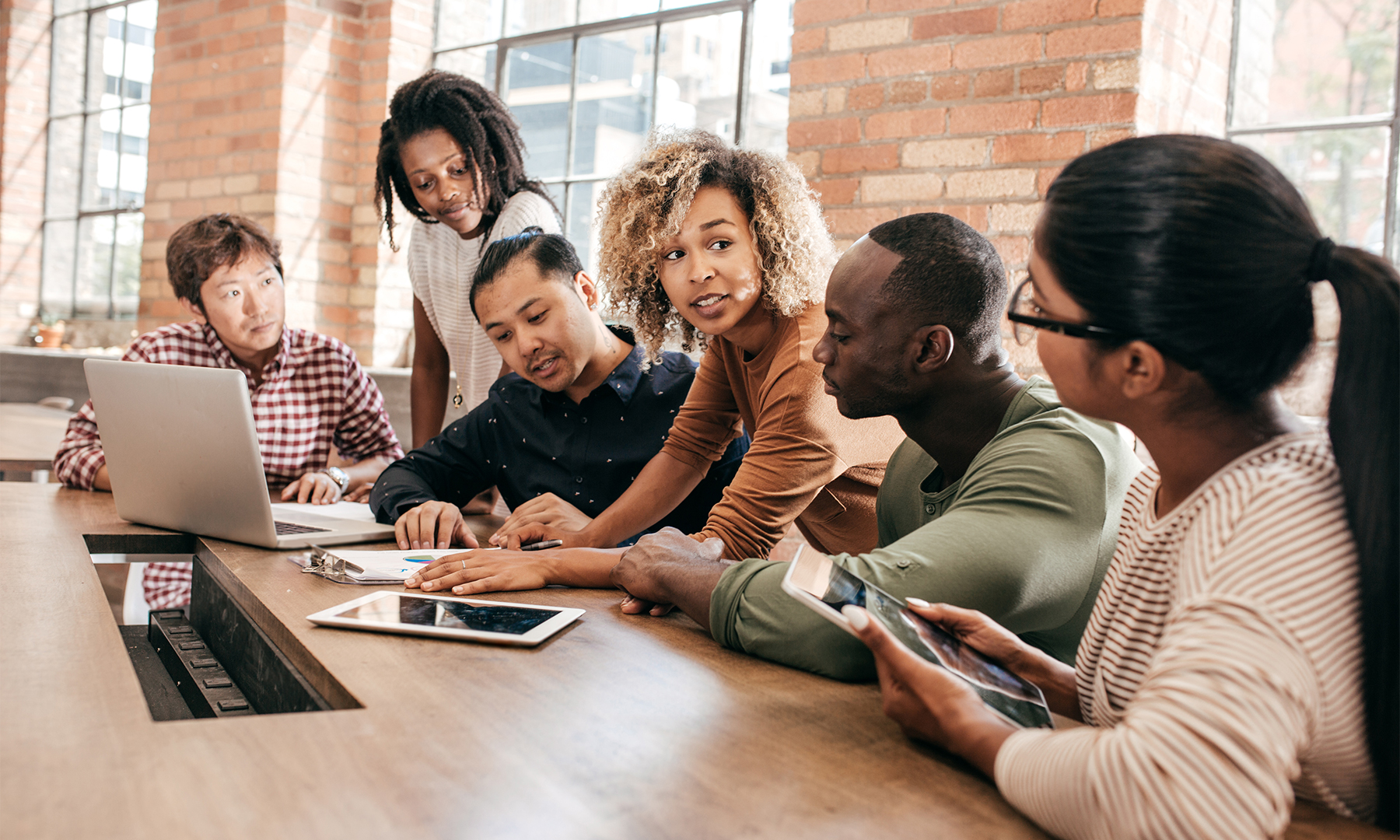 Group of professional led by woman of color gathered around documents.