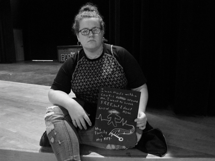 Young student holding sign that says "I was made with a cookie cutter around me. I want to break free, but I don