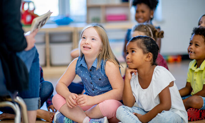 Two children, one of whom has a disability, sitting and listening to a teacher reading.