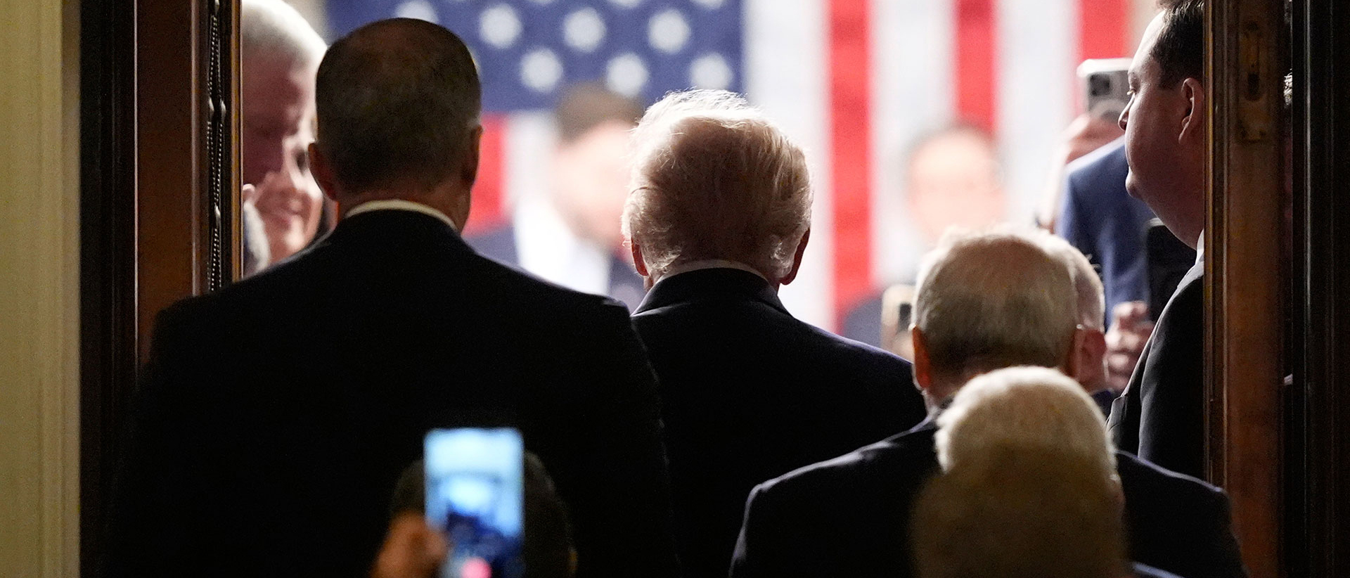 The back of several people in suits before an American flag.