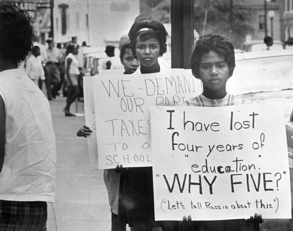People march in line with protest signs in an outdoor setting.