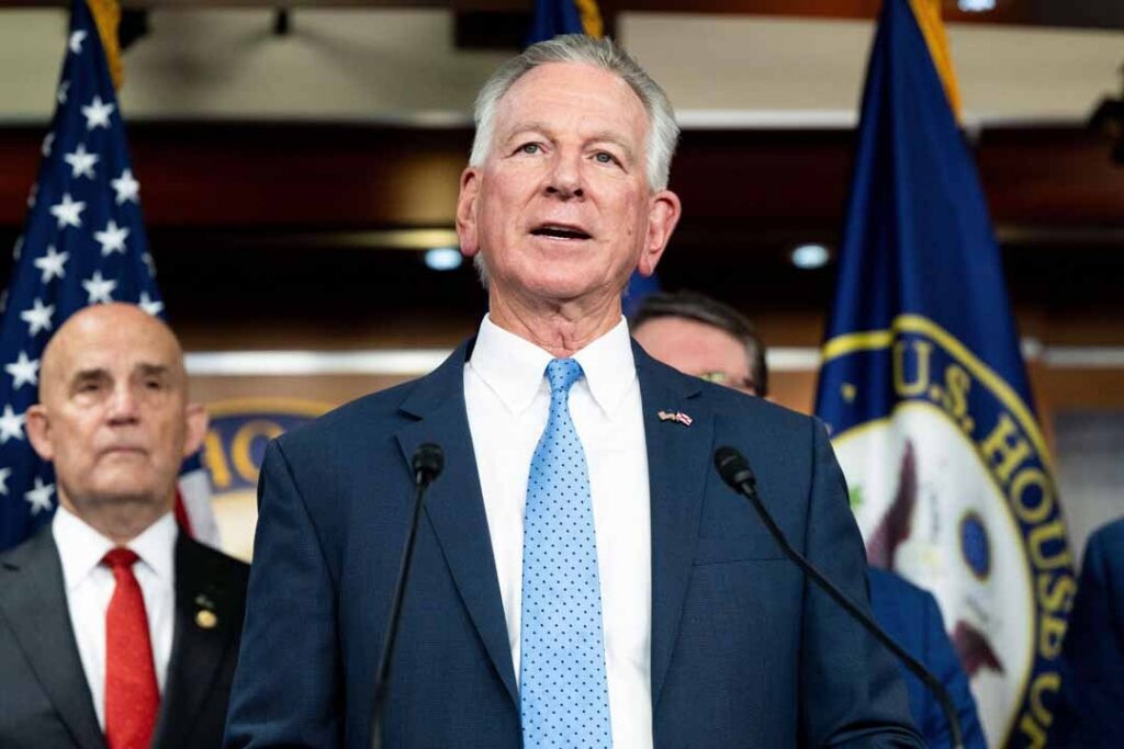 Person at podium flanked by flags in background.